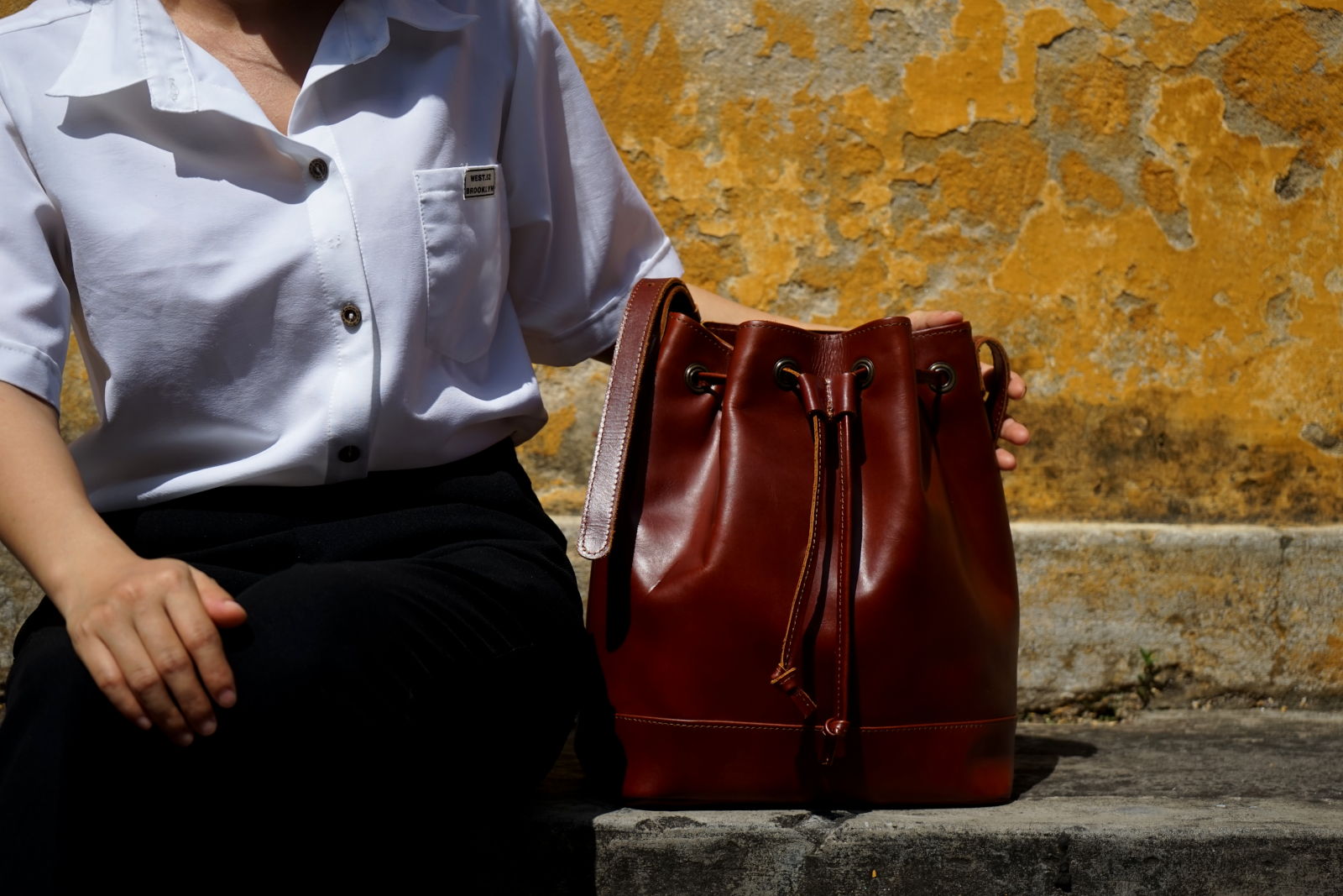Hoi An Real Leather - Da Bao Real Leather: Brown bucket bag in front of yellow wall in Hoi An Old Town