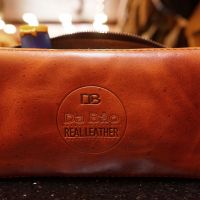 Real Leather Hoi An - Da Bao Real Leather: Front view of brown buffalo leather toiletry bag with Da Bao logo.